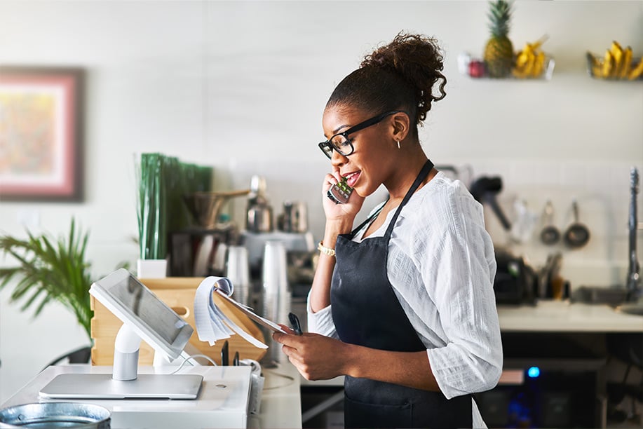 Friendly-waitress-taking-order-on-phone-at-restaurant-and-writing-on-notepad---Image